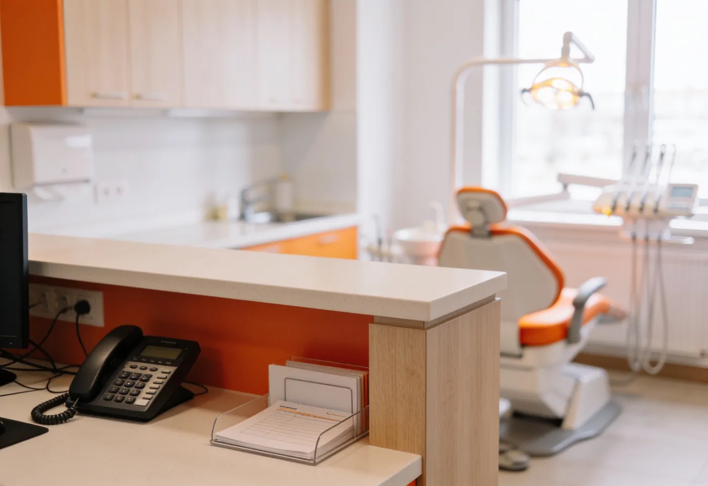 Comptoir d'accueil d'un cabinet dentaire avec le téléphone au premier plan et le fauteuil de soins en arrière-plan
